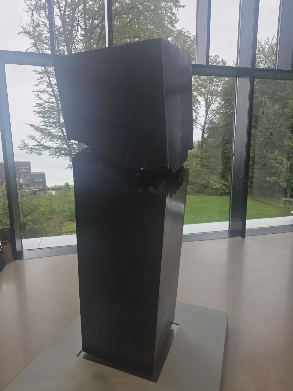 Ett högt mörkt skulpturalt verk av Filip Palmén står framför RAVINENs stora fönster med det gröna landskapet utanför.